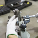 Technician in gloves uses a tool to measure a gear's spur size