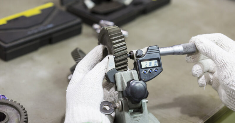 Technician in gloves uses a tool to measure a gear's spur size