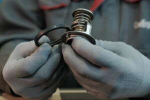An auto mechanic holds a thermostat and an O-ring in his hands. Control of the serviceability and conformity of parts. Replacing the O-ring on the thermostat at the car service station.