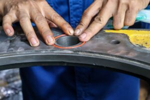 Close-up of a technician's hands carefully fitting a precision orange rubber O-ring gasket into a circular groove on a heavy-duty steel machine part.